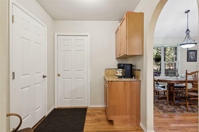 kitchen featuring light wood-type flooring, pendant lighting, light brown cabinets, and light stone countertops