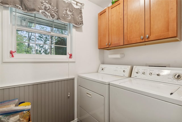 clothes washing area featuring wainscoting, cabinet space, and washing machine and clothes dryer