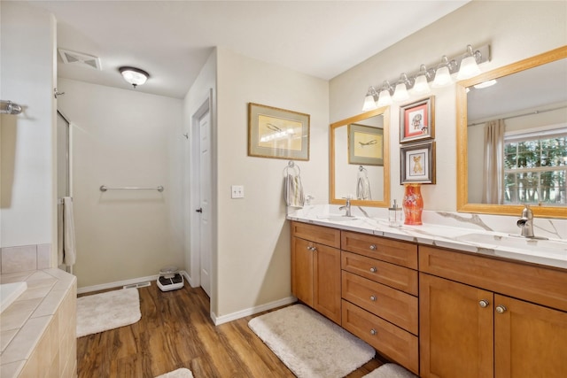 bathroom featuring double vanity, a sink, wood finished floors, tiled tub, and baseboards