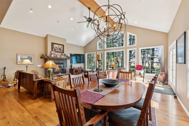 living room with ceiling fan with notable chandelier, light hardwood / wood-style flooring, a stone fireplace, and vaulted ceiling with beams