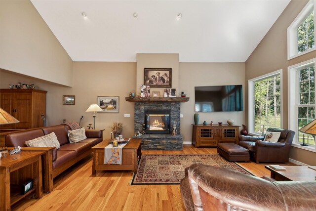 dining space with high vaulted ceiling, light wood-type flooring, a notable chandelier, and a stone fireplace