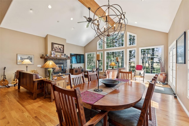 dining area with light wood-style floors, a notable chandelier, high vaulted ceiling, and a stone fireplace