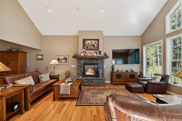 living room featuring high vaulted ceiling, light wood-type flooring, a healthy amount of sunlight, and a fireplace