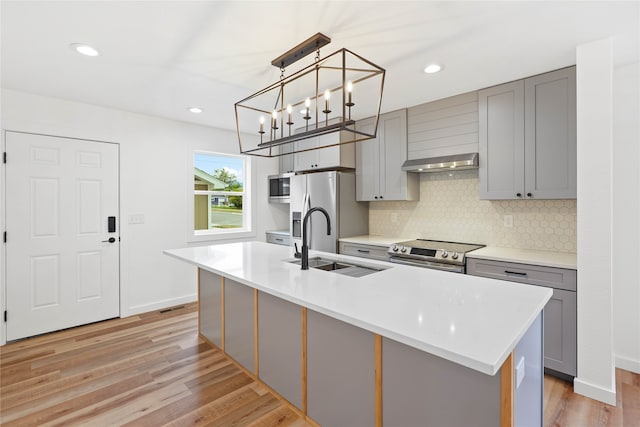 kitchen with decorative light fixtures, gray cabinets, a kitchen island with sink, and light hardwood / wood-style floors