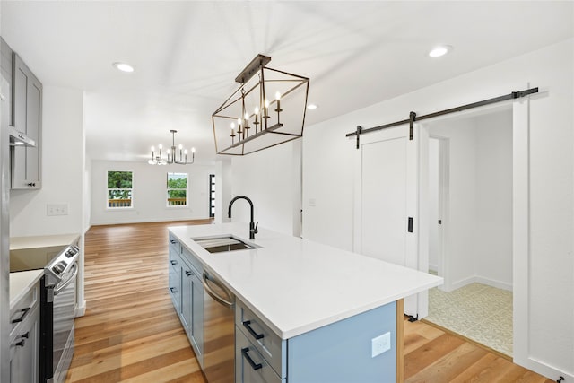 kitchen with sink, a barn door, light hardwood / wood-style floors, a kitchen island with sink, and appliances with stainless steel finishes