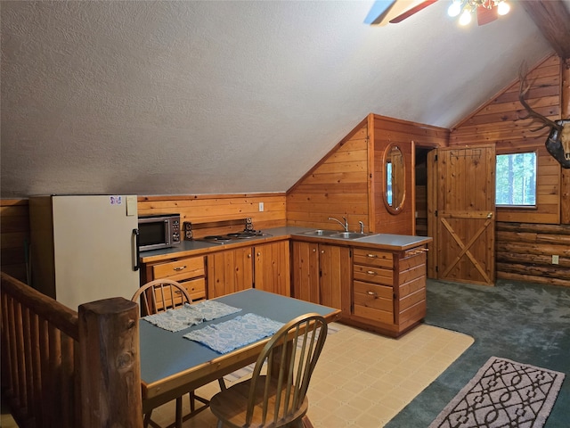 kitchen featuring vaulted ceiling, stainless steel appliances, a textured ceiling, wooden walls, and sink