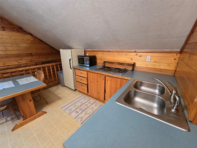 kitchen with a textured ceiling, sink, lofted ceiling, stainless steel appliances, and wooden walls