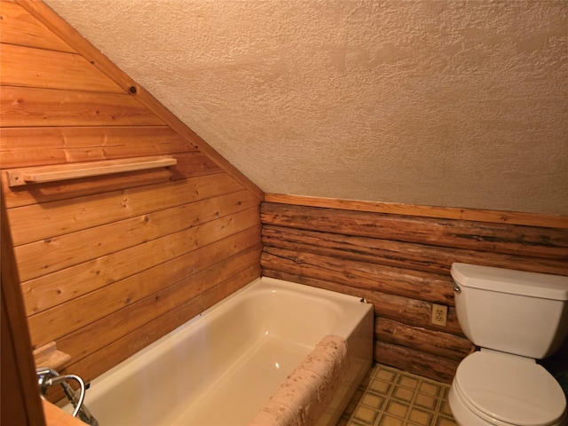 bathroom featuring a bathtub, a textured ceiling, wooden walls, and toilet