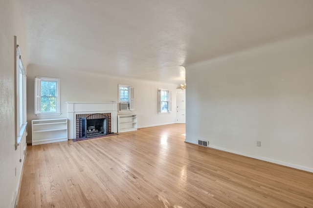 unfurnished living room featuring a notable chandelier, a brick fireplace, light wood-style flooring, baseboards, and visible vents
