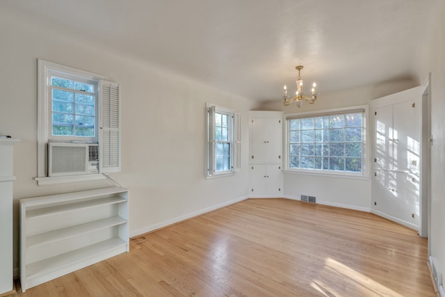 spare room with an inviting chandelier, plenty of natural light, and light hardwood / wood-style floors