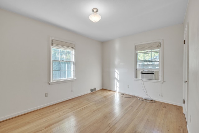unfurnished room featuring cooling unit, light wood-style flooring, visible vents, and a healthy amount of sunlight
