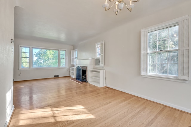 unfurnished living room featuring a fireplace with flush hearth, visible vents, baseboards, wood finished floors, and a notable chandelier