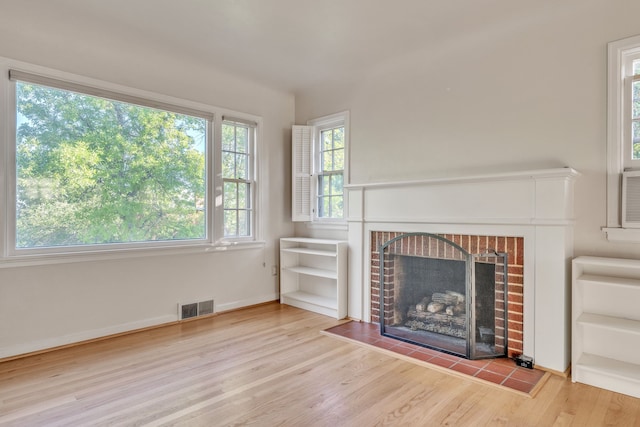 unfurnished living room featuring visible vents, a brick fireplace, and wood finished floors