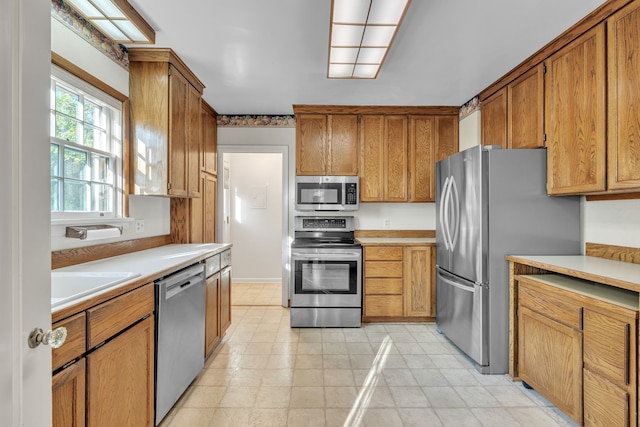 kitchen featuring light countertops, a sink, appliances with stainless steel finishes, and brown cabinetry