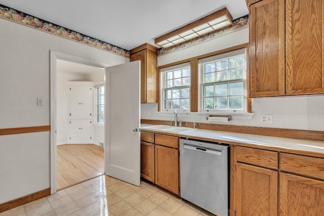 kitchen with light countertops, a sink, dishwasher, brown cabinets, and baseboards
