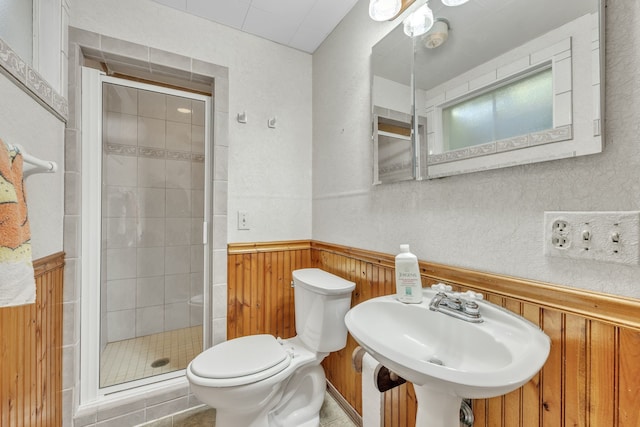 bathroom featuring a stall shower, toilet, a sink, wood walls, and wainscoting