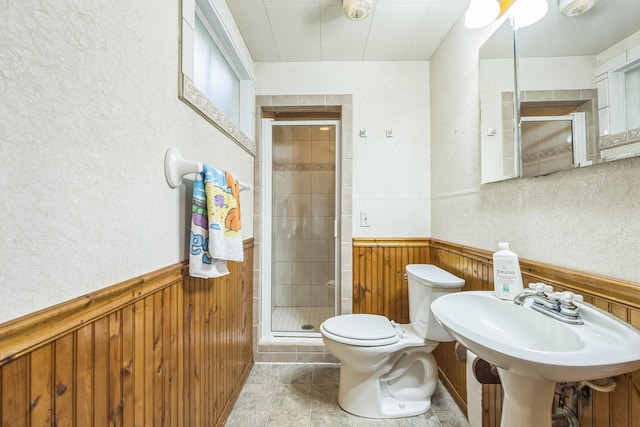 bathroom featuring toilet, a sink, a shower stall, wooden walls, and wainscoting