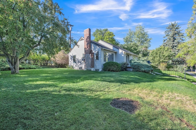 view of side of property featuring fence, a yard, and a chimney