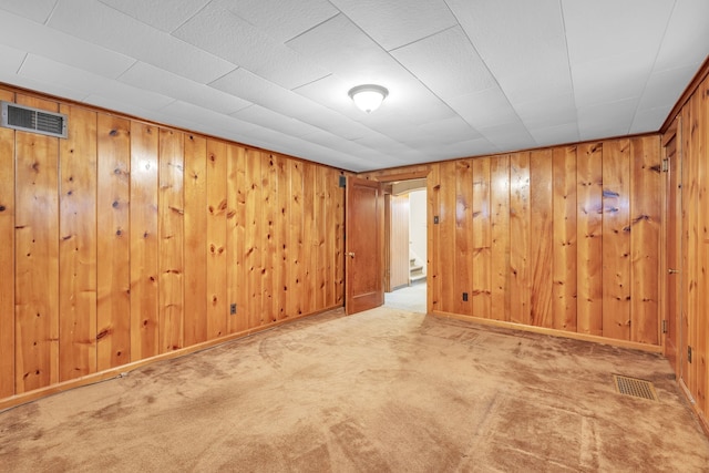 carpeted empty room with baseboards, visible vents, and wood walls