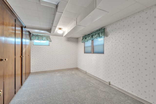 basement with baseboards, wallpapered walls, a drop ceiling, and carpet