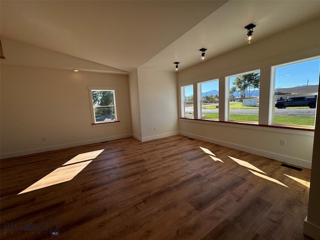 empty room with lofted ceiling, plenty of natural light, and dark hardwood / wood-style flooring