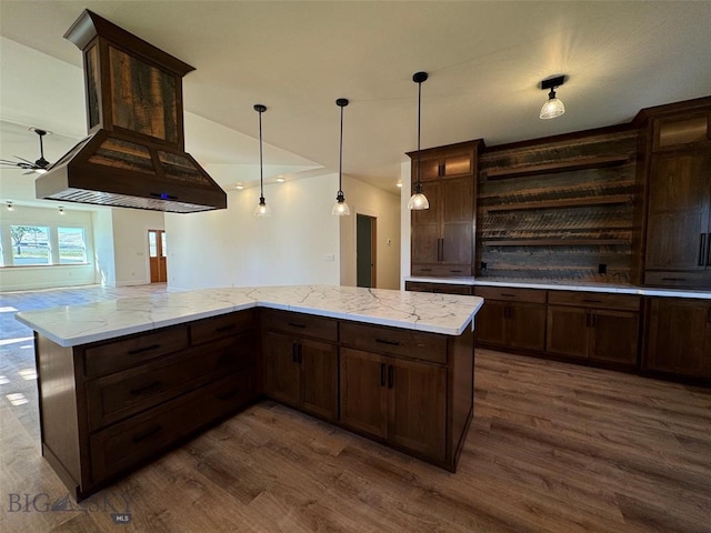 kitchen with pendant lighting, dark wood-type flooring, dark brown cabinetry, light stone countertops, and ceiling fan