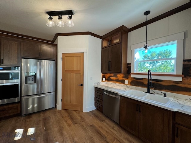 kitchen featuring hanging light fixtures, sink, hardwood / wood-style flooring, appliances with stainless steel finishes, and light stone countertops