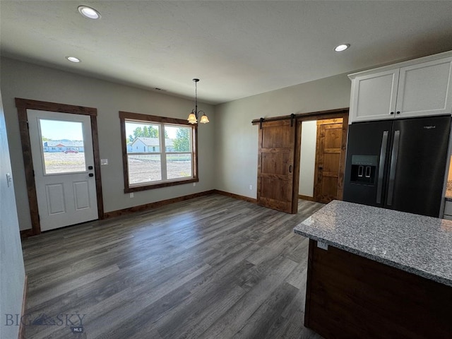 kitchen with white cabinetry, a barn door, light stone countertops, dark hardwood / wood-style floors, and black fridge