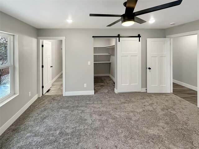 unfurnished bedroom with ceiling fan, carpet flooring, a barn door, and a spacious closet