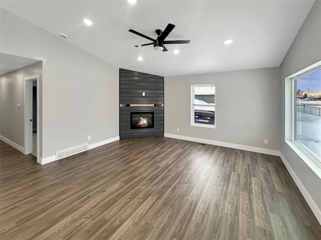 unfurnished living room with dark wood-type flooring, a large fireplace, plenty of natural light, and ceiling fan