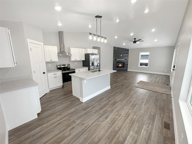 kitchen with appliances with stainless steel finishes, white cabinets, hanging light fixtures, a center island with sink, and wall chimney exhaust hood