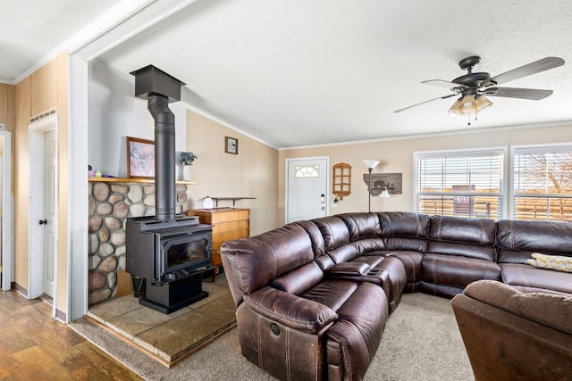 living room with a wood stove, hardwood / wood-style flooring, ornamental molding, ceiling fan, and a textured ceiling