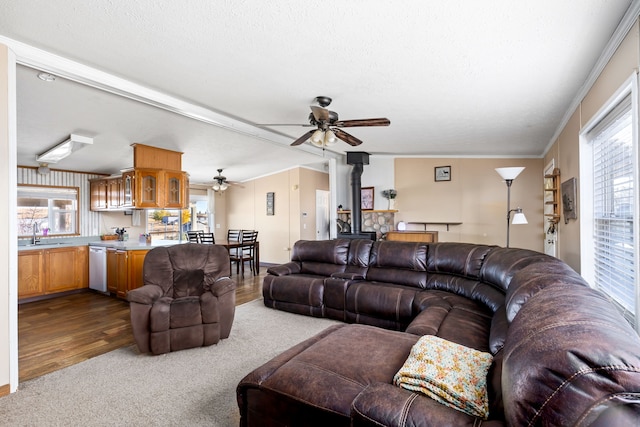 living room featuring sink, crown molding, ceiling fan, dark colored carpet, and a wood stove