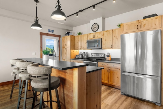 kitchen featuring light brown cabinets, hanging light fixtures, appliances with stainless steel finishes, and light hardwood / wood-style flooring