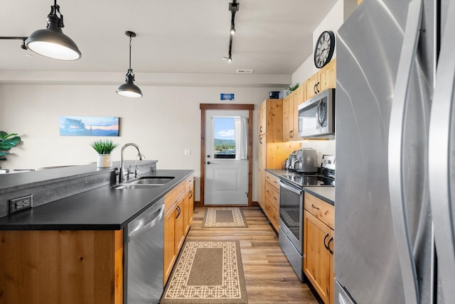 kitchen featuring appliances with stainless steel finishes, track lighting, sink, light hardwood / wood-style flooring, and hanging light fixtures