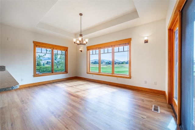 empty room with a mountain view, light hardwood / wood-style floors, a raised ceiling, and a chandelier