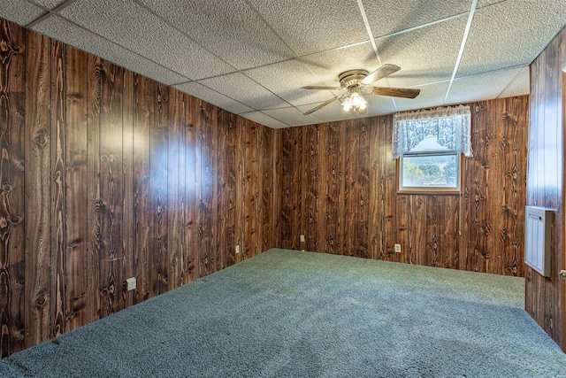 carpeted spare room with wooden walls and ceiling fan