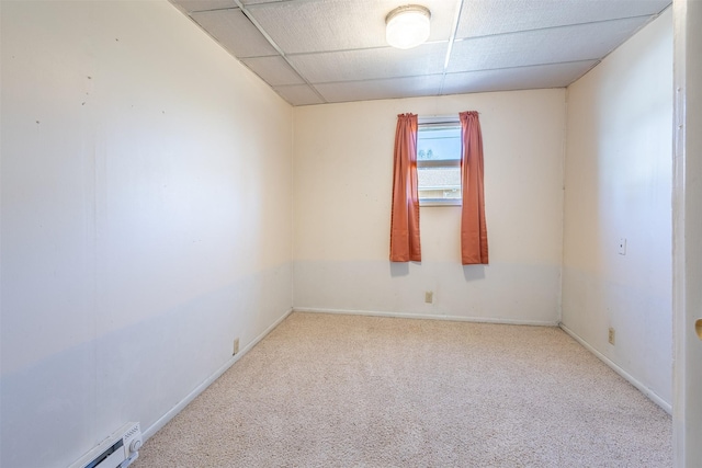 carpeted empty room featuring baseboard heating, baseboards, and a drop ceiling