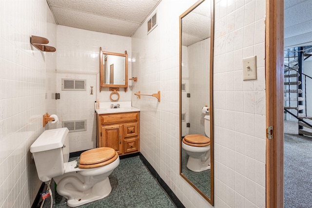 bathroom with tile walls, toilet, vanity, and visible vents