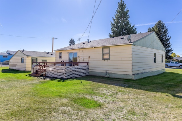 back of property with roof with shingles, a wooden deck, and a lawn
