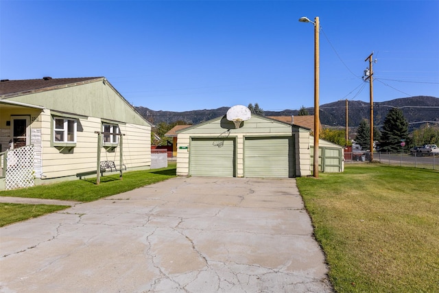 view of side of home featuring a lawn, fence, a mountain view, and an outbuilding