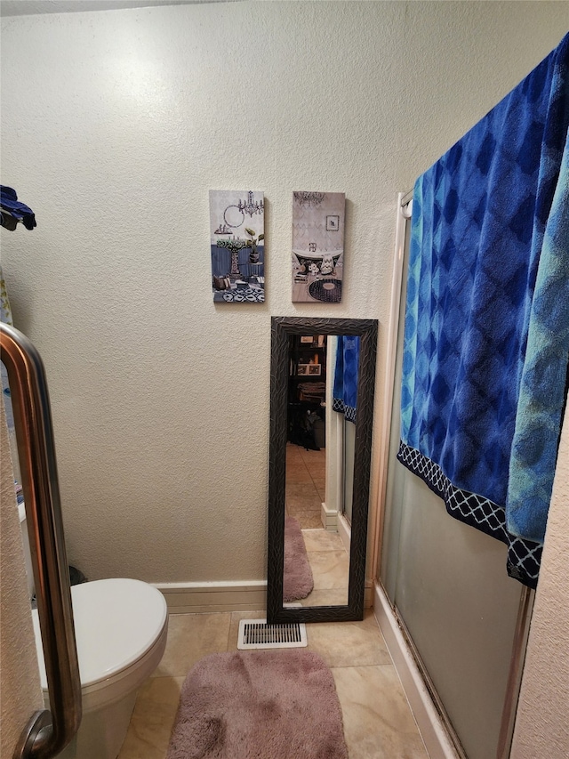 bathroom with a shower with door, toilet, and tile patterned floors