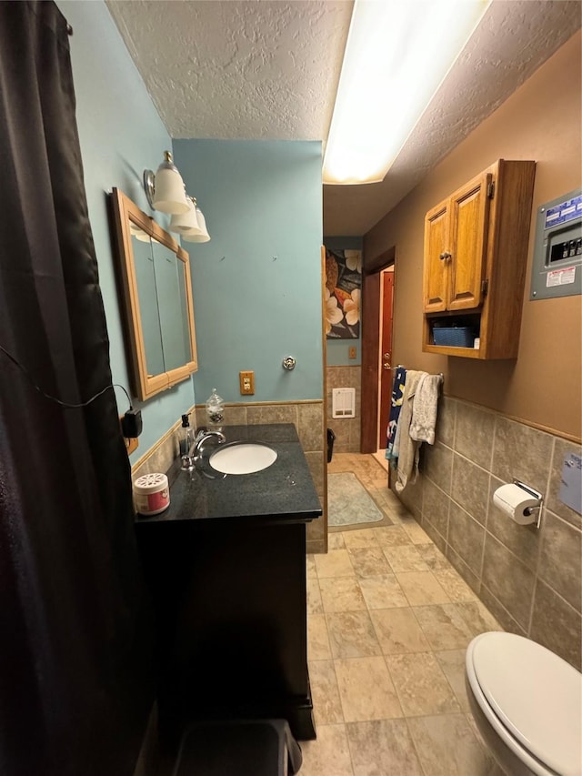 bathroom with vanity, toilet, tile walls, a textured ceiling, and a wainscoted wall