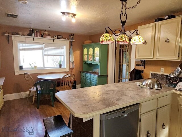 kitchen featuring stainless steel dishwasher, wood-type flooring, decorative light fixtures, and tile countertops