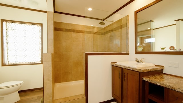 bathroom featuring hardwood / wood-style floors, crown molding, tiled shower, vanity, and toilet