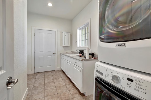 laundry area with sink, stacked washer / drying machine, cabinets, and light tile patterned flooring