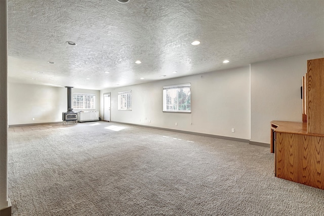 unfurnished living room with light carpet, a wood stove, and a textured ceiling