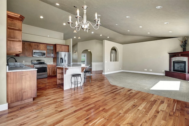 kitchen featuring appliances with stainless steel finishes, light wood-type flooring, vaulted ceiling, sink, and a center island