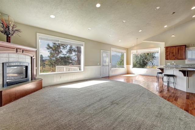 unfurnished living room with light hardwood / wood-style floors, a textured ceiling, lofted ceiling, and a tile fireplace