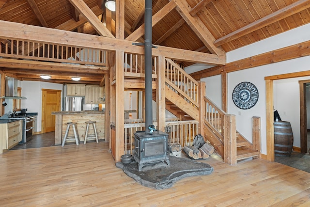 living room featuring beamed ceiling, light hardwood / wood-style flooring, a wood stove, and high vaulted ceiling